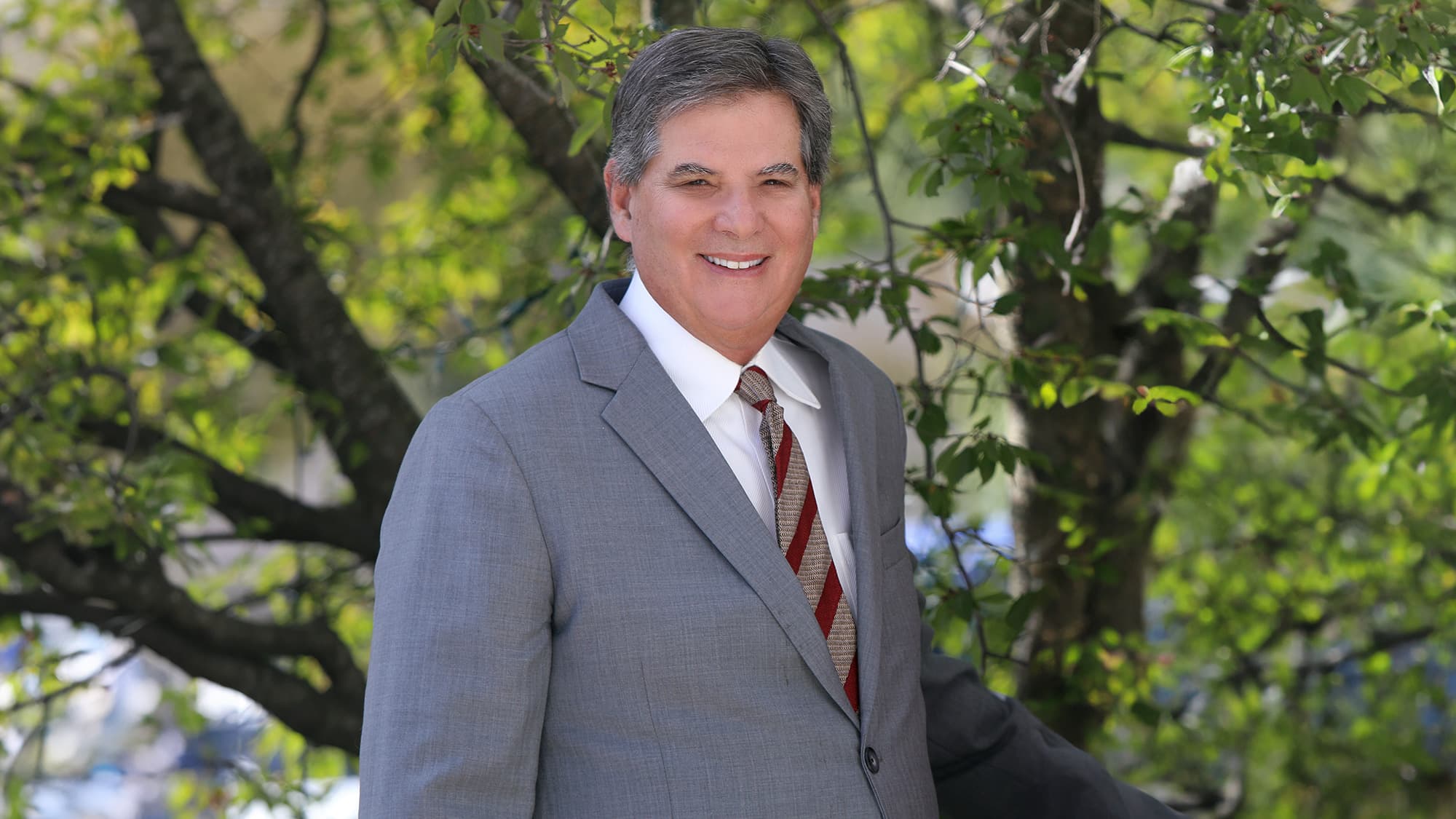 Dr. Mandell-Brown standing outside in from of green foliage smiling and posing for the camera